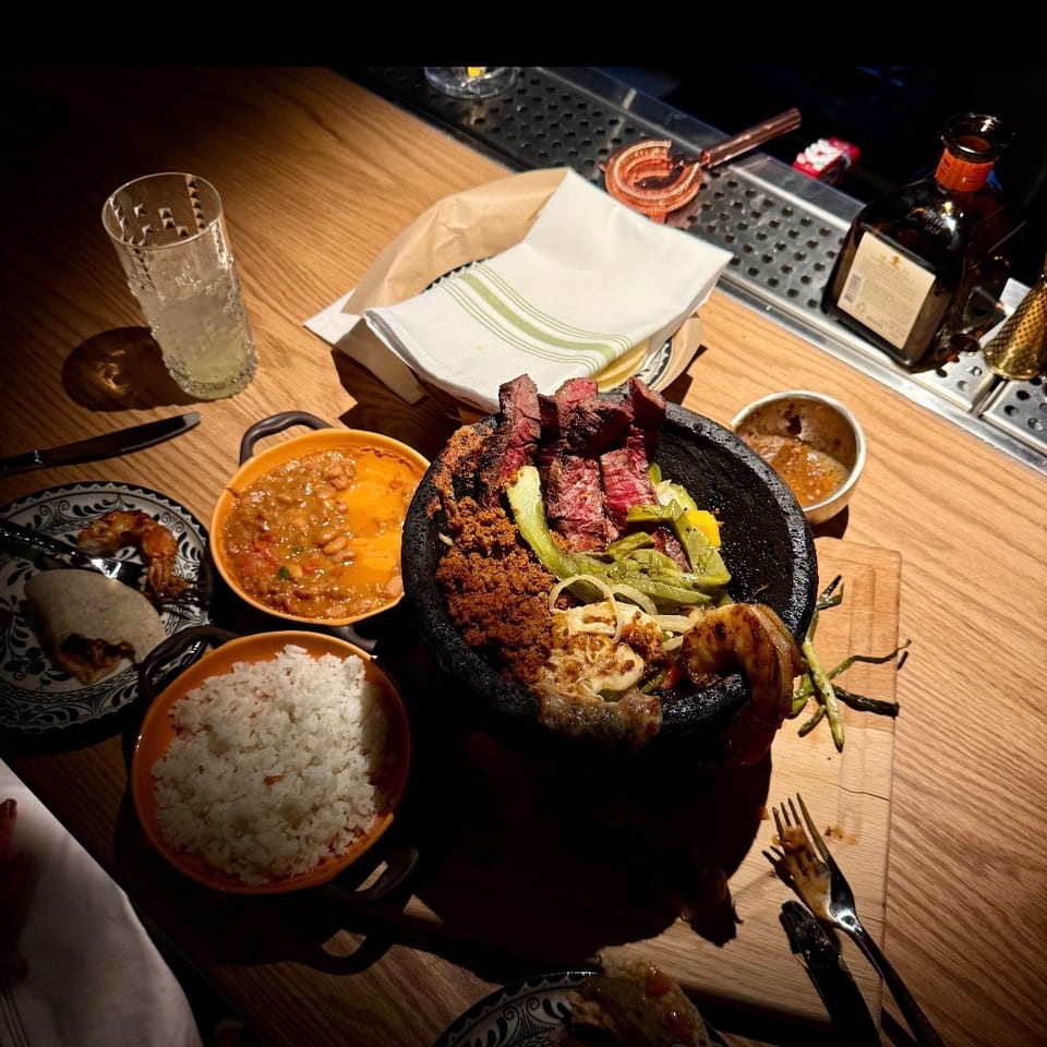 Vibrant Mexican-style meal with sliced grilled steak, vegetables, rice, beans, tortillas, and sauces served on a wooden restaurant table.